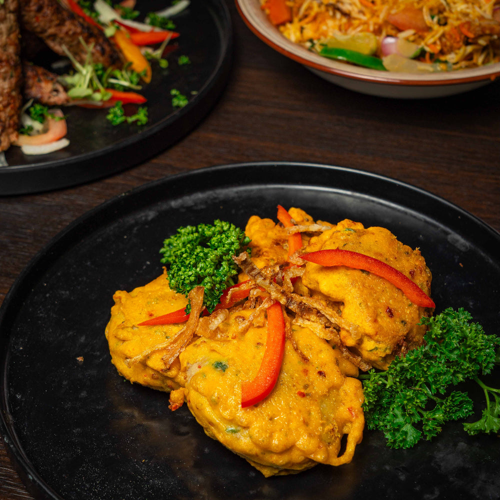 Plated dish of yellow curry with vegetables on a dark plate, surrounded by other dishes.