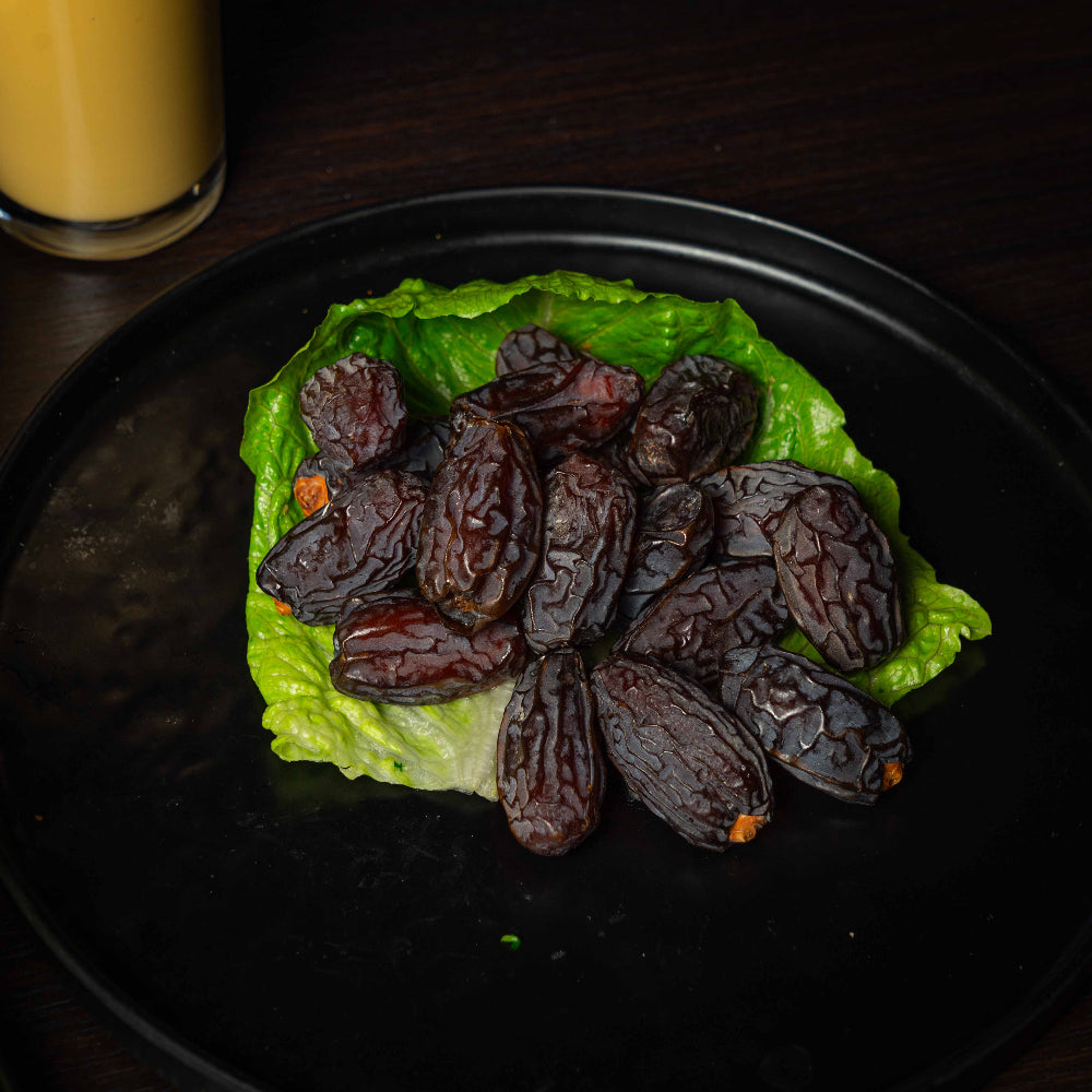 Dates on a bed of lettuce on a black plate with a glass of orange juice in the background.