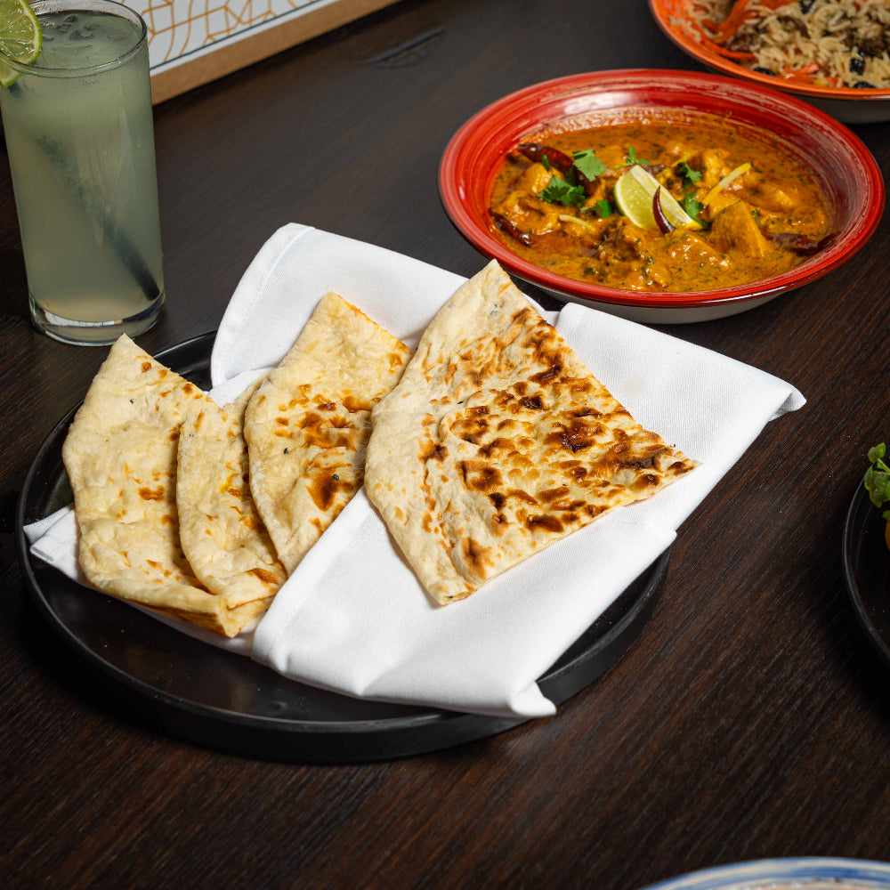 Plates of flatbread and a bowl of curry on a wooden table